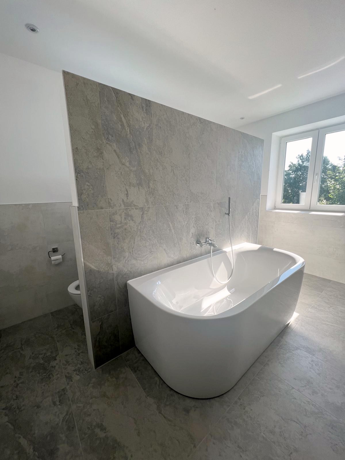 Bad mit Steinoptik und freistehender Wanne am Fenster